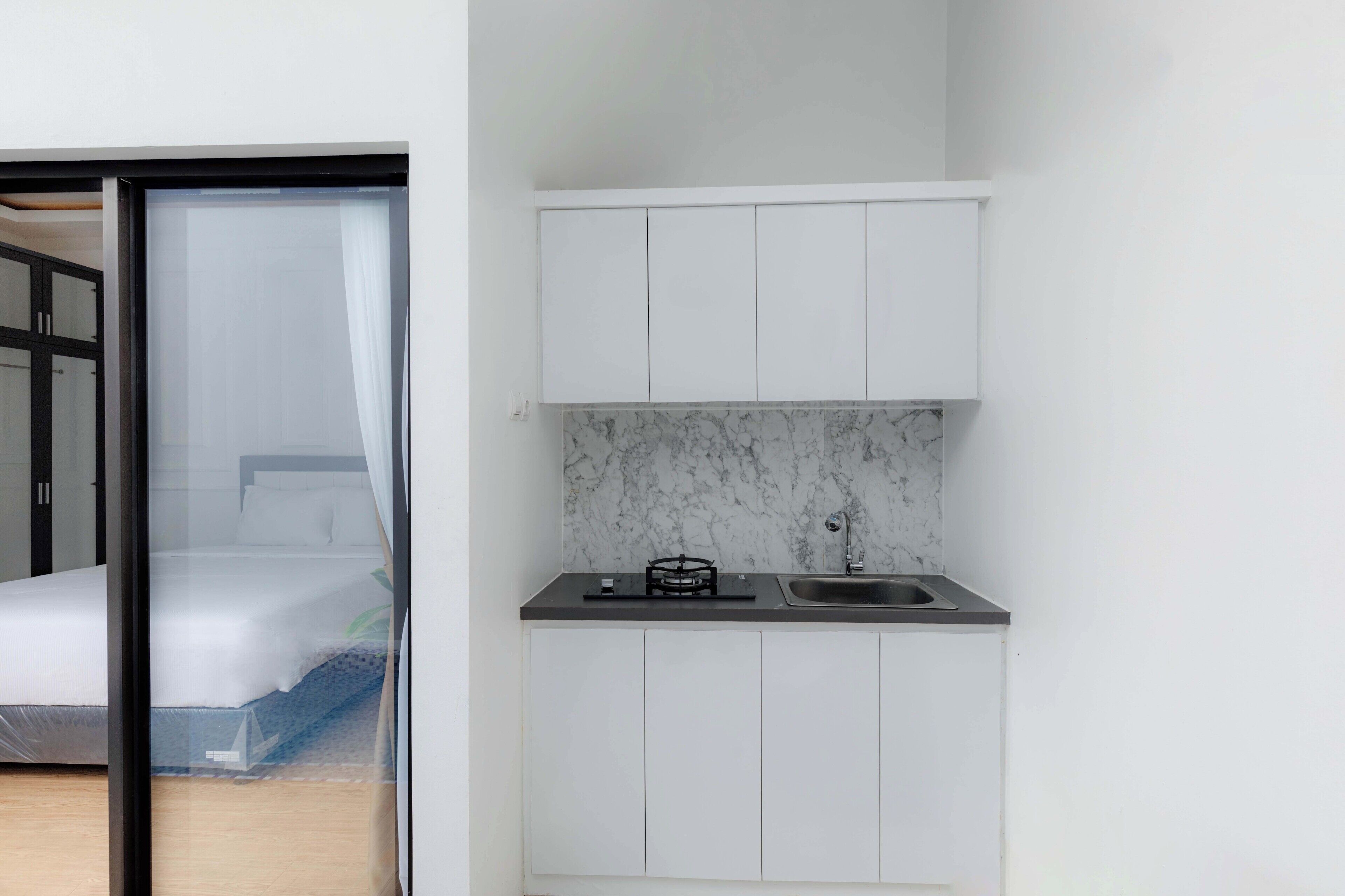 A compact kitchen with white cabinets, a marble backsplash, and a black countertop.