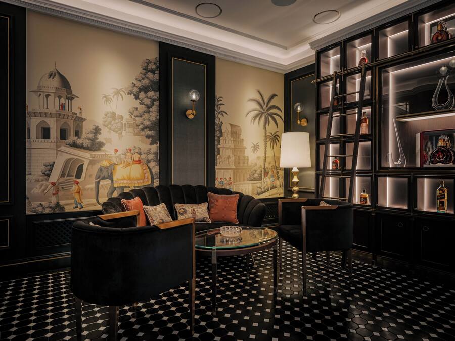Ein luxuriöser Raum mit einem schwarz-weiß karierten Boden, einem schwarzen Sofa mit gemusterten Kissen, einem Glastisch und einer Wand mit einem großen Wandgemälde.