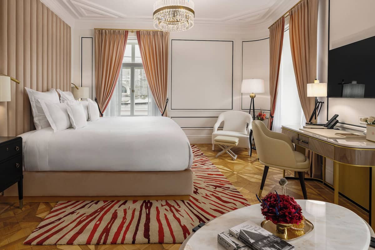 A hotel room with a large bed, a desk with a chair, a television, and a chandelier.