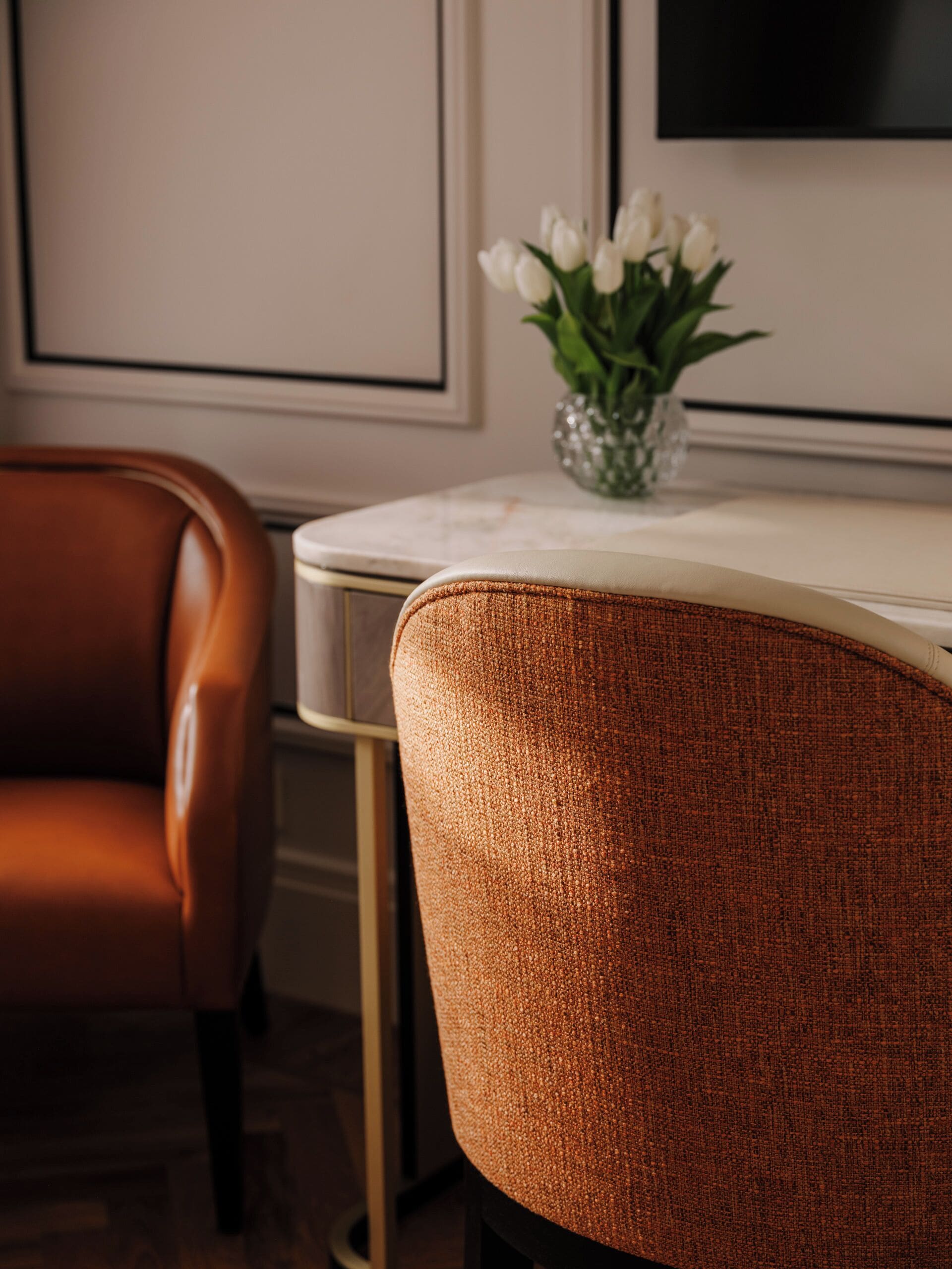 A dining area with a brown leather chair, a white table, and a vase with white flowers.