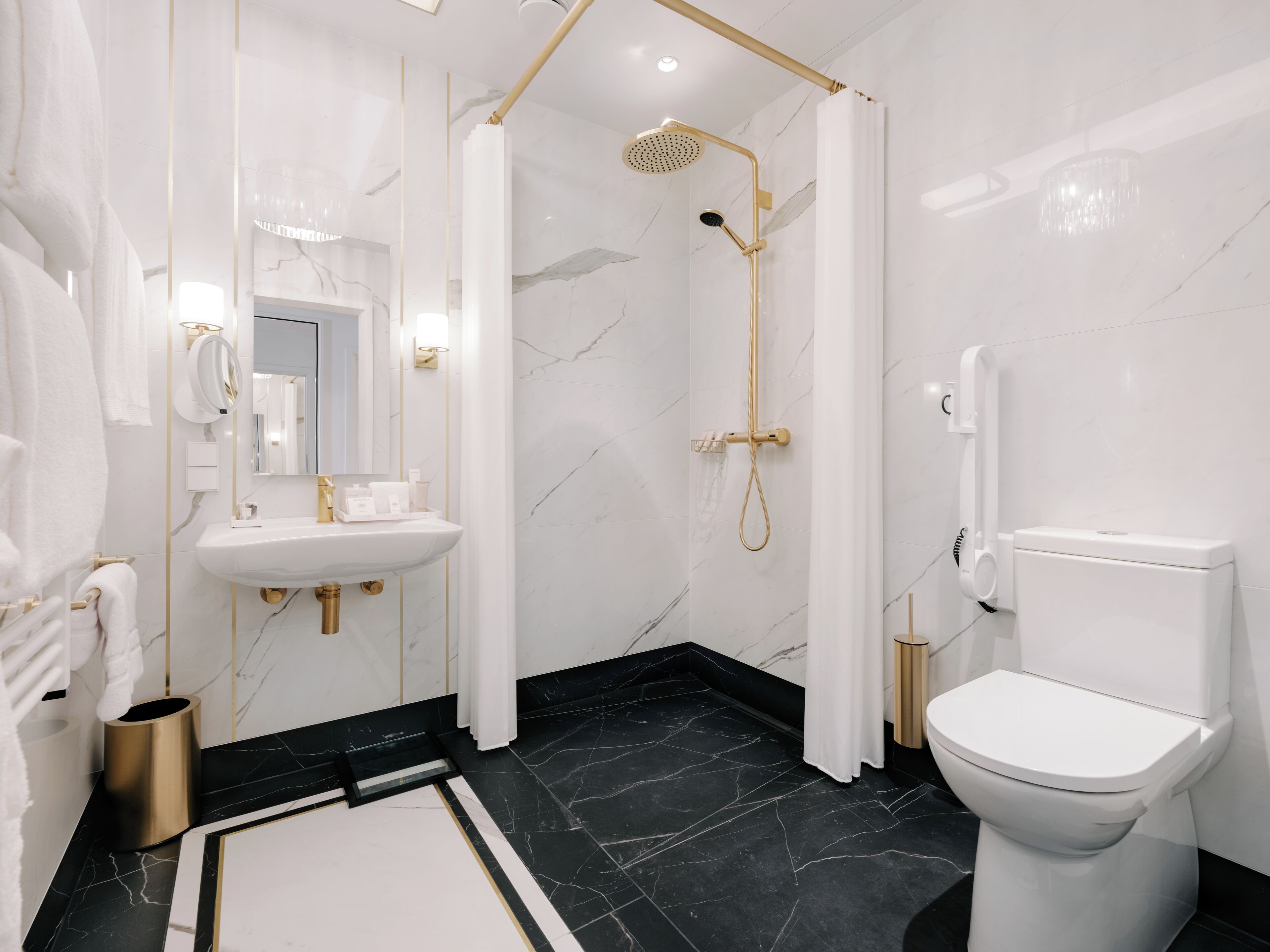 Une salle de bain moderne avec un lavabo blanc, des robinetteries dorées, un sol en marbre noir et des toilettes blanches.