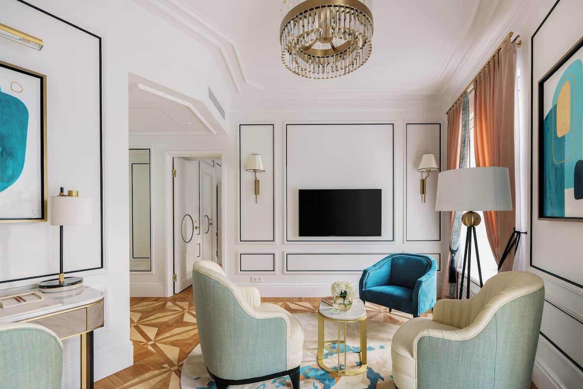 A modern living room with a flat-screen TV, two armchairs, a coffee table, and a chandelier.
