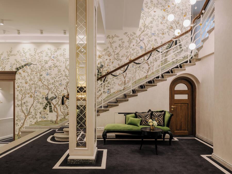 Una imponente escalera con papel tapiz floral, un sofá verde y una puerta de madera.