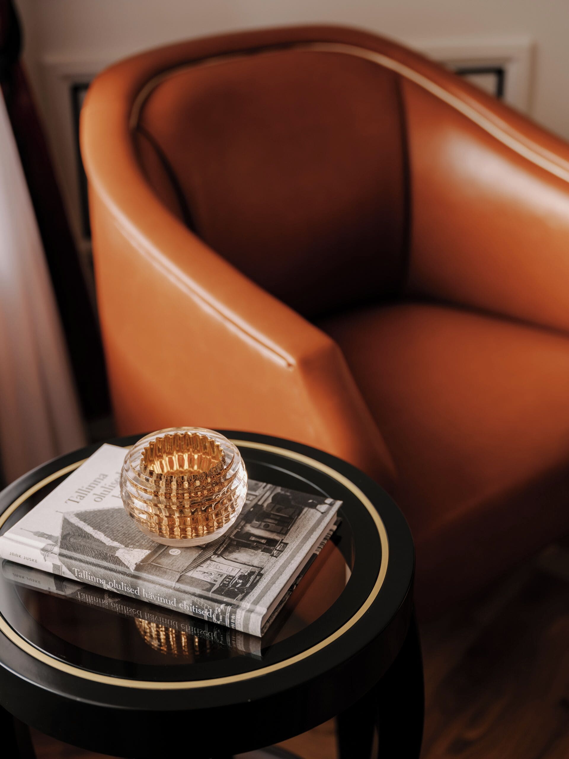A brown leather armchair, a black side table with a gold decorative object, and a book titled 'Tallinna' on the table.