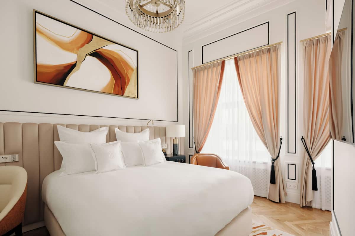 A modern hotel room with a large bed, a chair, a desk, and a chandelier.