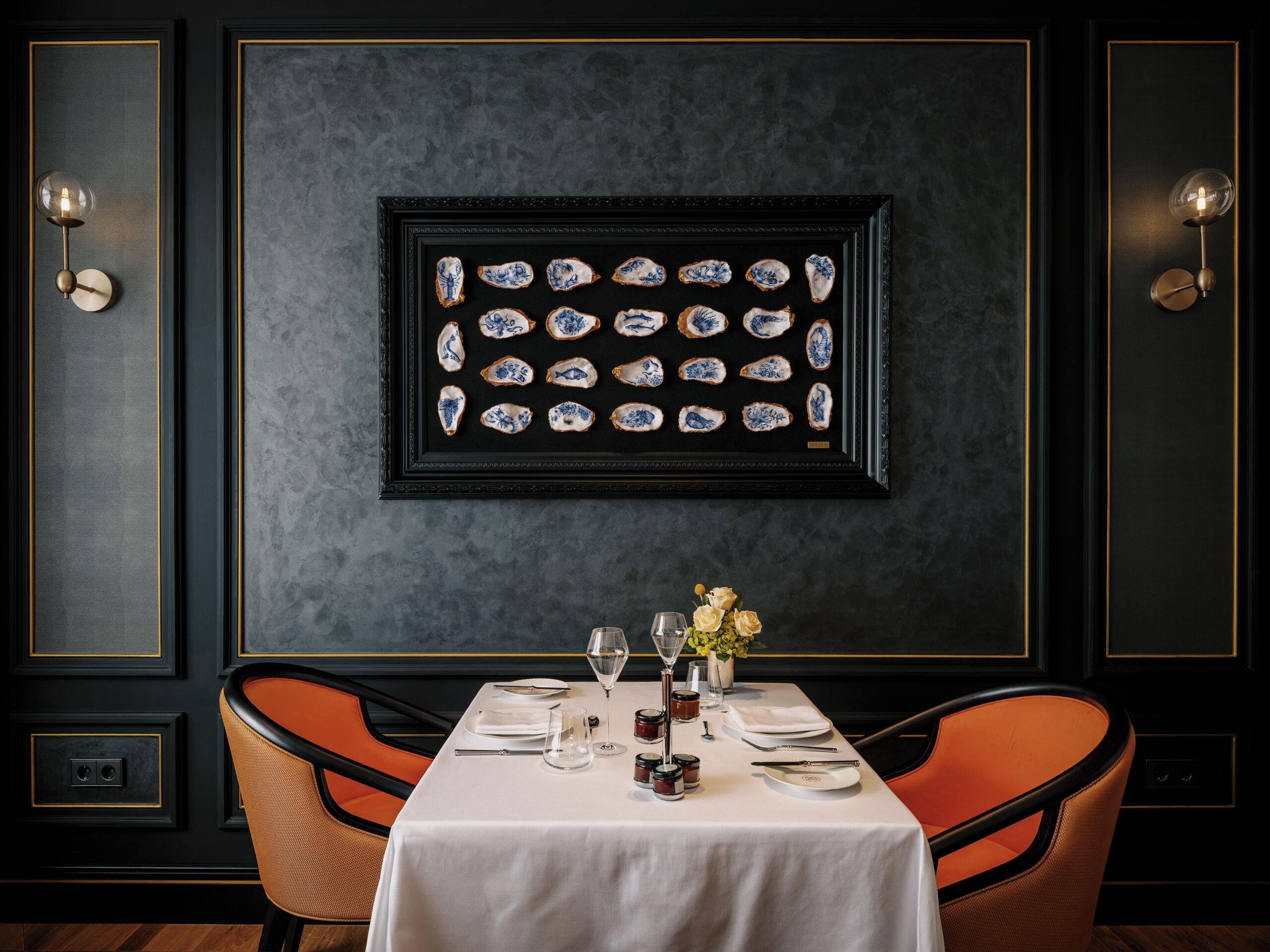 Ein Esszimmer mit Tisch für zwei Personen, Bildern über dem Tisch und Wandleuchten.