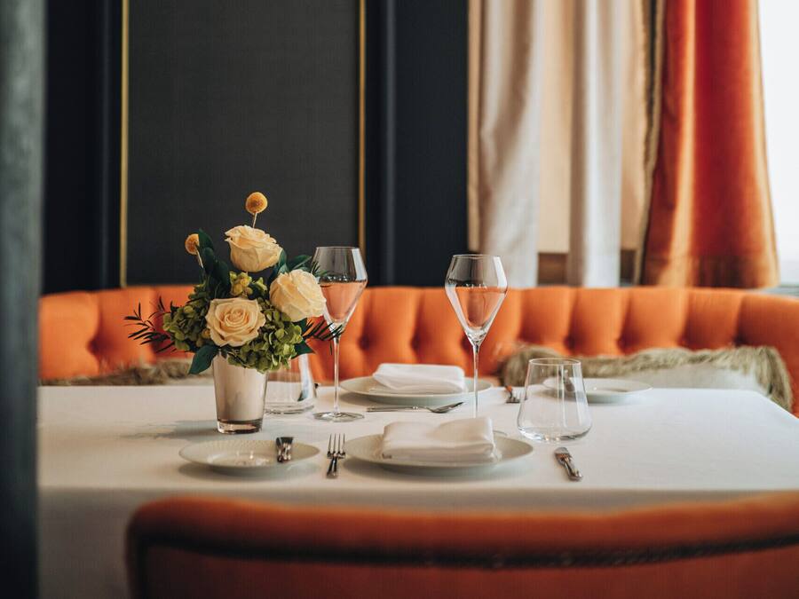 A dining table set with white plates, silverware, and a vase with white flowers.