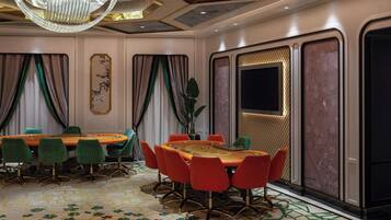 Une salle de conférence dotée d’une grande table ovale, de chaises vertes et rouges, d’un lustre et d’un tapis à motifs.