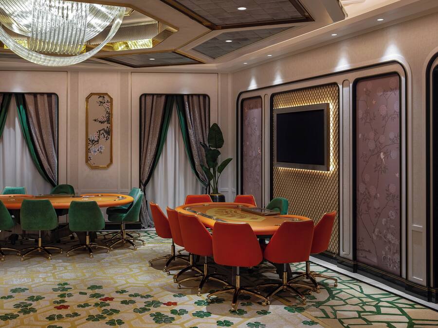 Une salle de conférence dotée d’une grande table ovale, de chaises vertes et rouges, d’un lustre et d’un tapis à motifs.