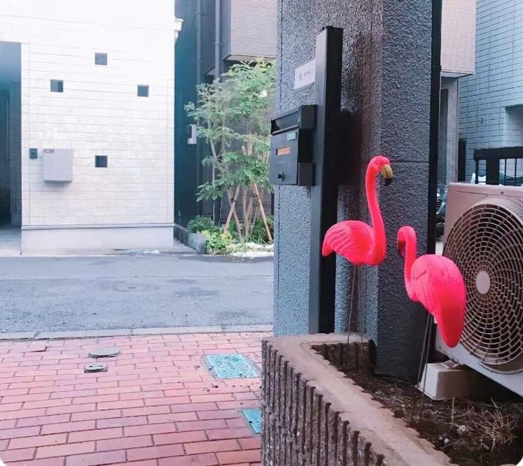 A building entrance with a brick pathway, a metal gate, and a red flamingo decoration.