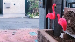 Une entrée d’immeuble avec un chemin en briques, un portail en métal et une décoration représentant un flamant rose.