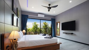 Une chambre d’hôtel moderne dotée d’un grand lit, d’un ventilateur de plafond, d’un téléviseur à écran plat et offrant une vue sur les palmiers par la fenêtre.