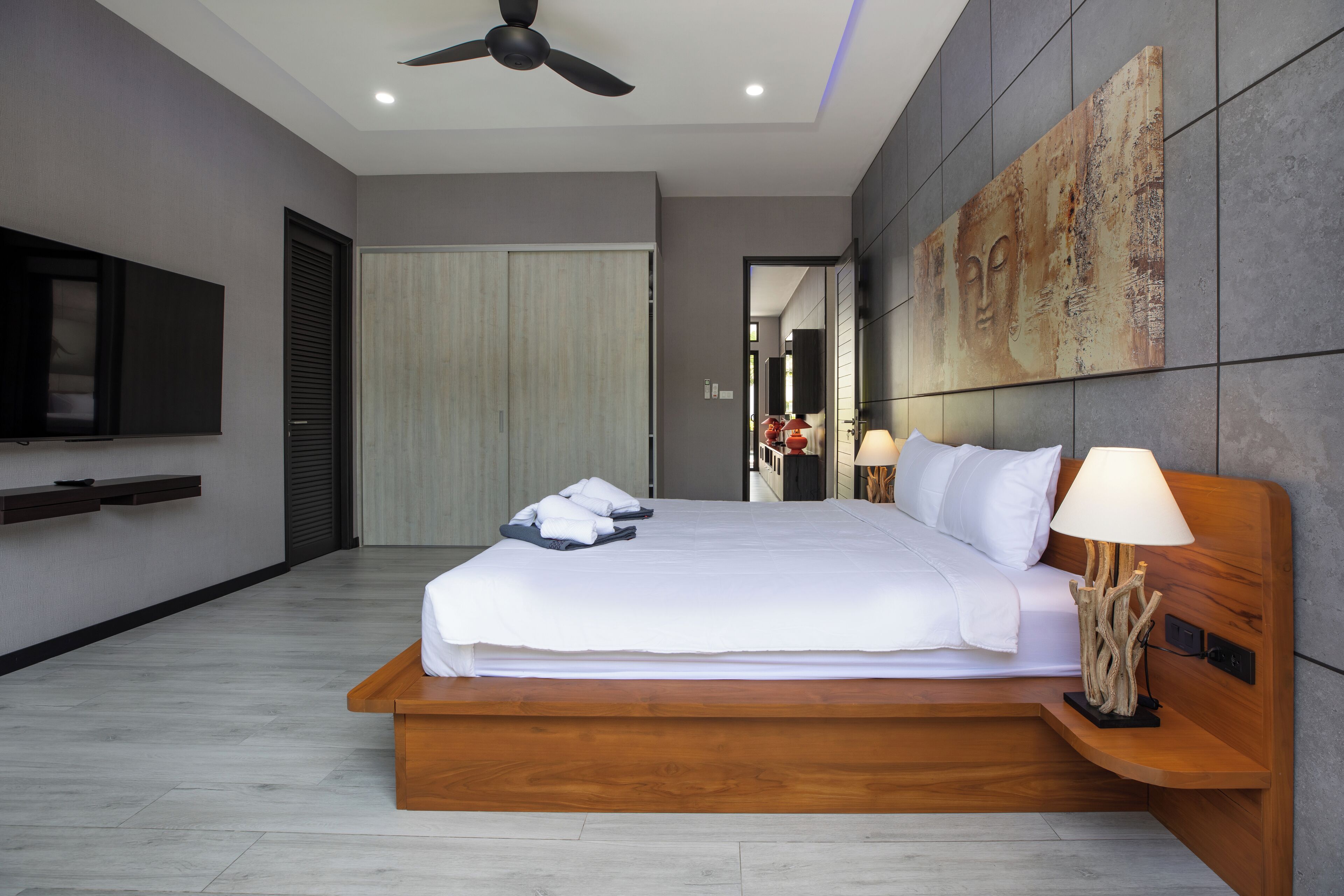 A modern hotel room with a large bed, a flat-screen TV, a ceiling fan, and a large artwork on the wall.