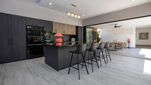 Une cuisine moderne avec des meubles de couleur sombre, un îlot central doté de tabourets, et un coin repas avec une table et des chaises.