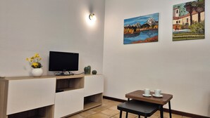 Una habitación pequeña con un televisor sobre un mueble de madera, una mesita con dos tazas y dos cuadros en la pared.