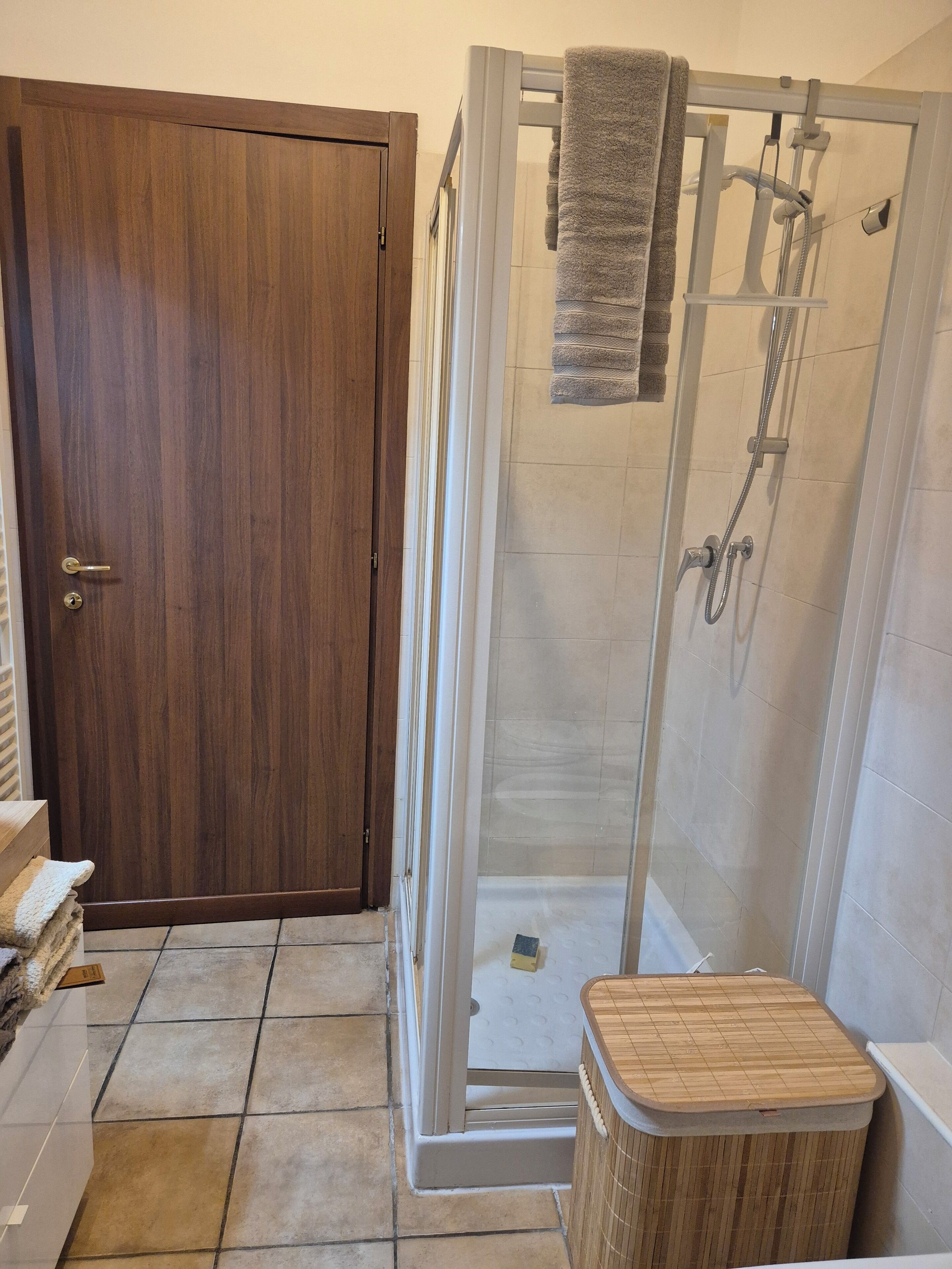 Ein Badezimmer mit Holztür, einer Duschkabine aus Glas und einem kleinen Holzschemel.