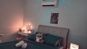 A bedroom with a bed, bedside table, nightstand, and a wall-mounted air conditioner.