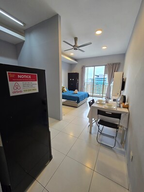 A hotel room with a bed, a desk with a chair, a ceiling fan, and a view of the city through large windows. - Neo Mutiara Damansara Studio 2PAX 1CP (Petaling Jaya)