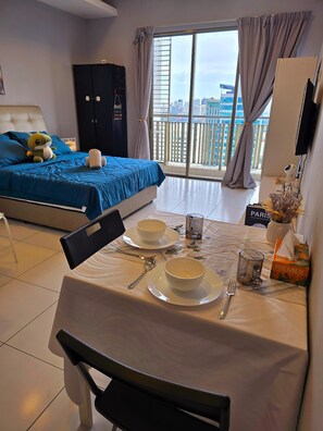 A hotel room with a bed, a dining table set with plates and bowls, a chair, and a view of a cityscape through large windows. - Neo Mutiara Damansara Studio 2PAX 1CP (Petaling Jaya)
