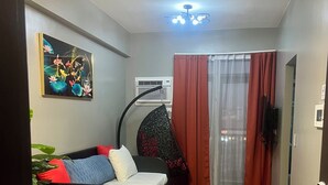 A compact living space with a bed, a dining table, a hanging chair, and a ceiling fan. - Cozy 1-bedroom condo with WiFi, AC near OKADA HOTEL Paranaque (Parañaque)
