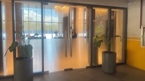 A modern reception area with glass doors, potted plants, and a view of the outdoors. - Cozy 1-bedroom condo with WiFi, AC near OKADA HOTEL Paranaque (Parañaque)