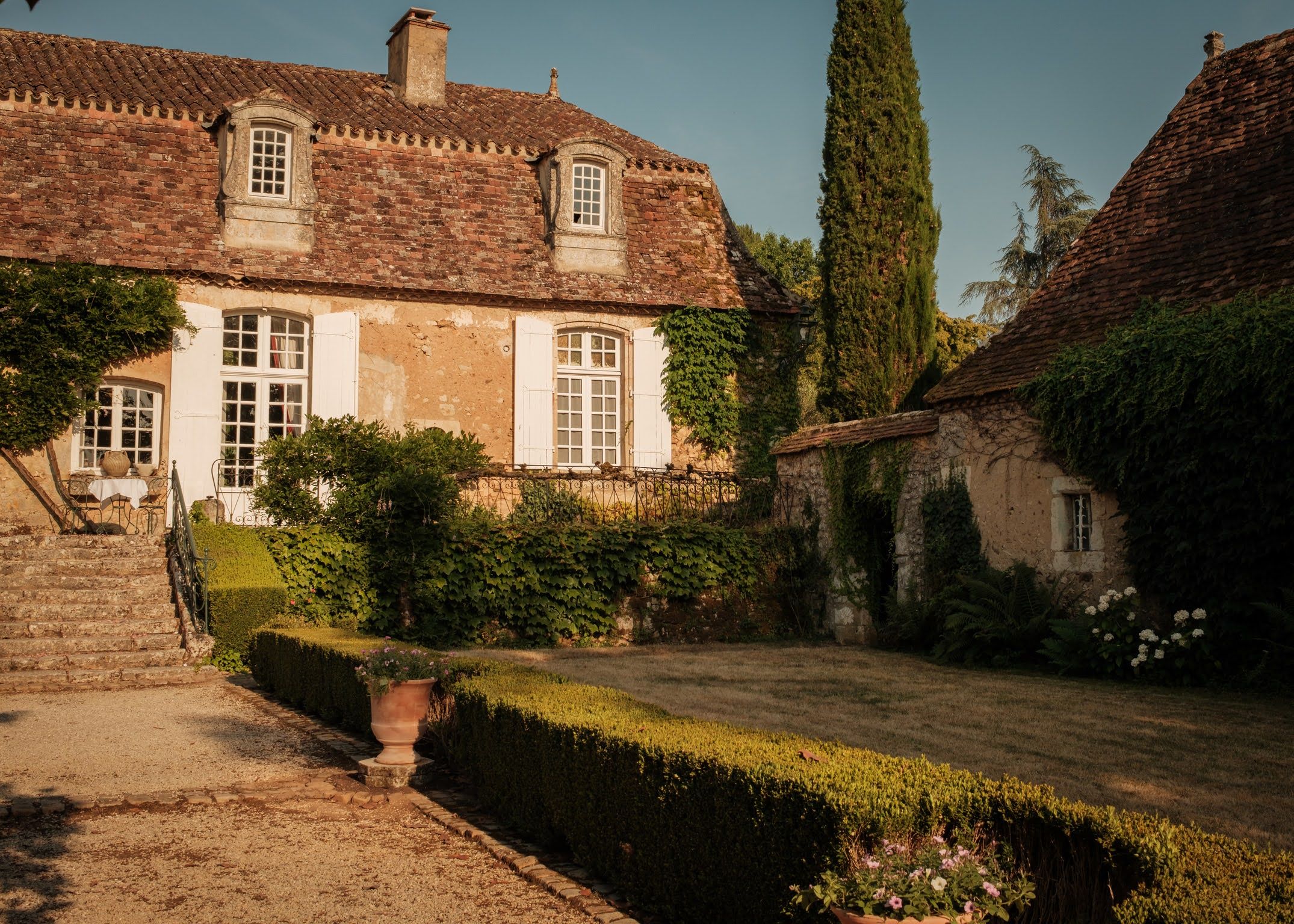 Una casa tradicional de ladrillo con un jardín cuidado, un árbol alto y un cielo despejado.