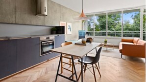 A modern kitchen with a large island, a dining area with a table and chairs, and a view of greenery through large windows. - NYC Studio in Central Oslo (Oslo)
