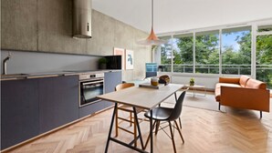 A modern kitchen with a large island, a dining area with a table and chairs, and a living space with a sofa and a view of greenery. - NYC Studio in Central Oslo (Oslo)