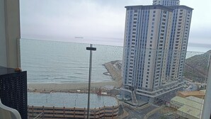 Een balkon met twee stoelen, uitzicht op een strand, een hoog gebouw en een weg met voertuigen.