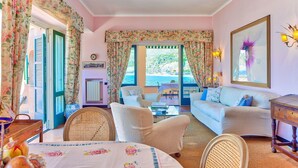 Un salon chaleureux avec un canapé, des fauteuils, une table avec des livres et une vue sur la mer grâce à de grandes fenêtres.