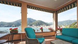 Un balcon agrémenté de meubles en osier, de plantes en pot et offrant une vue sur la mer et les montagnes.
