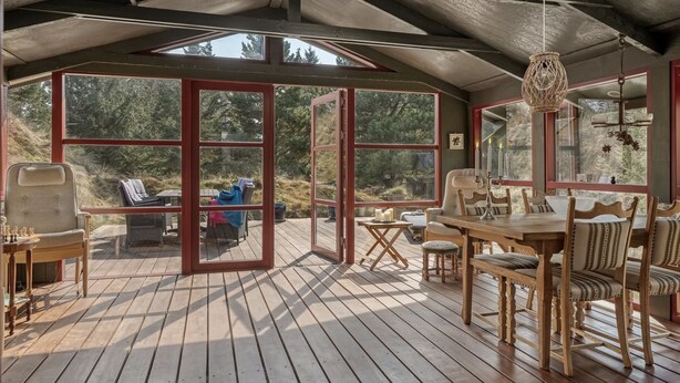 A covered deck with wooden flooring, a dining table with chairs, and a view of the surrounding forest. - "Nimrod" - 800m from the sea by Interhome (Blokhus)