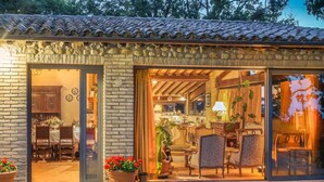 Un edificio de piedra tradicional con tejado de tejas, puertas de cristal grandes y un interior acogedor con muebles de madera y plantas en macetas.