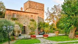 Un edificio de piedra con un jardín que incluye un sendero de piedra, plantas en macetas y una zona de barbacoa.