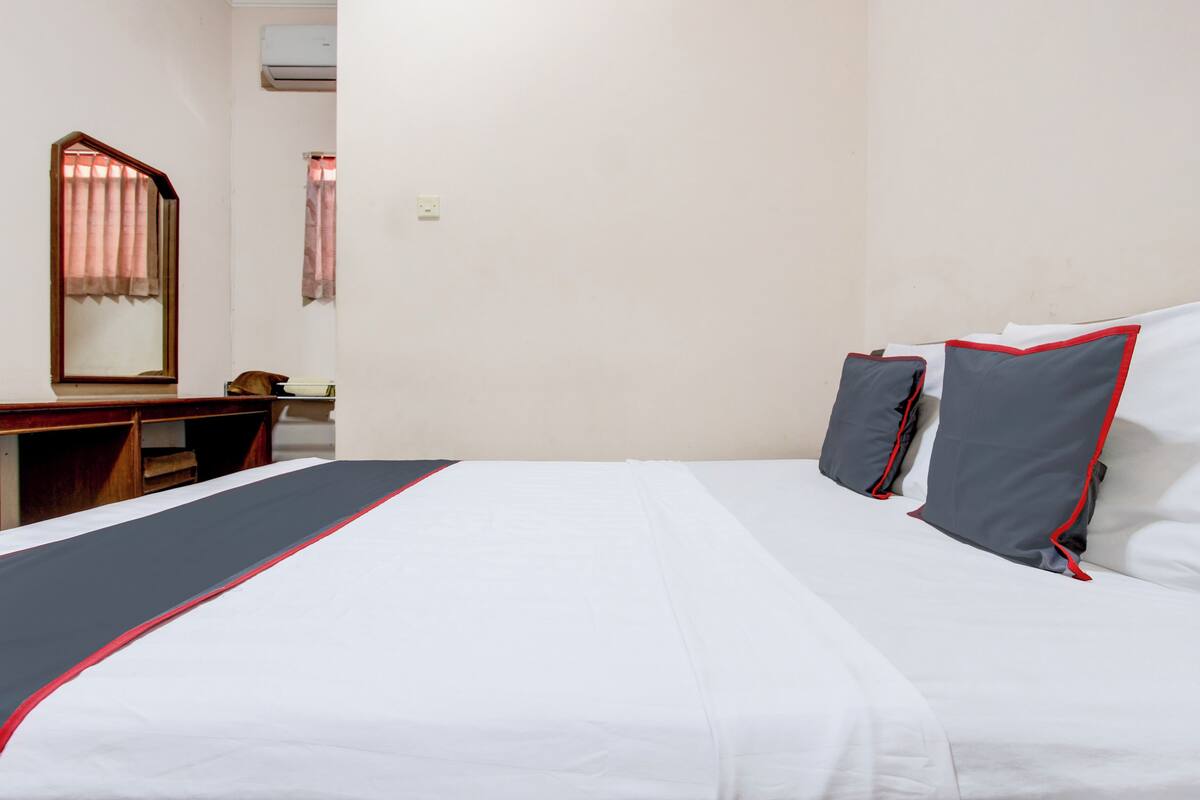 Une chambre d’hôtel avec un lit, un bureau, un miroir et une fenêtre avec des rideaux.