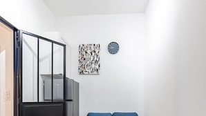 A compact living space with a kitchenette, a blue sofa, a glass table, and a blue chair. - 1#Cosystudio#Paris13#JardinDesPlantes (Paris)