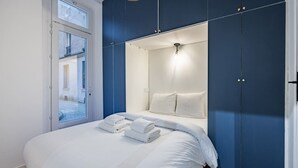 A modern bedroom with a large bed, a built-in wardrobe, and a window with a view of the outside. - 1#Cosystudio#Paris13#JardinDesPlantes (Paris)