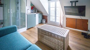A compact room with a sofa, a laundry basket, a kitchenette, and a TV mounted on the wall. - Studio FullEquiped 2person with balcony 17th (Paris)