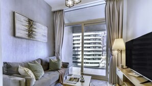 A modern living room with a grey sofa, a flat-screen TV, a coffee table, and a large window with a view of high-rise buildings. - Manzil-1BR w Canal View near Dubai Mall (Dubai)
