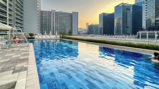 A rooftop pool with a cityscape view, surrounded by high-rise buildings. - Manzil-1BR w Canal View near Dubai Mall (Dubai)