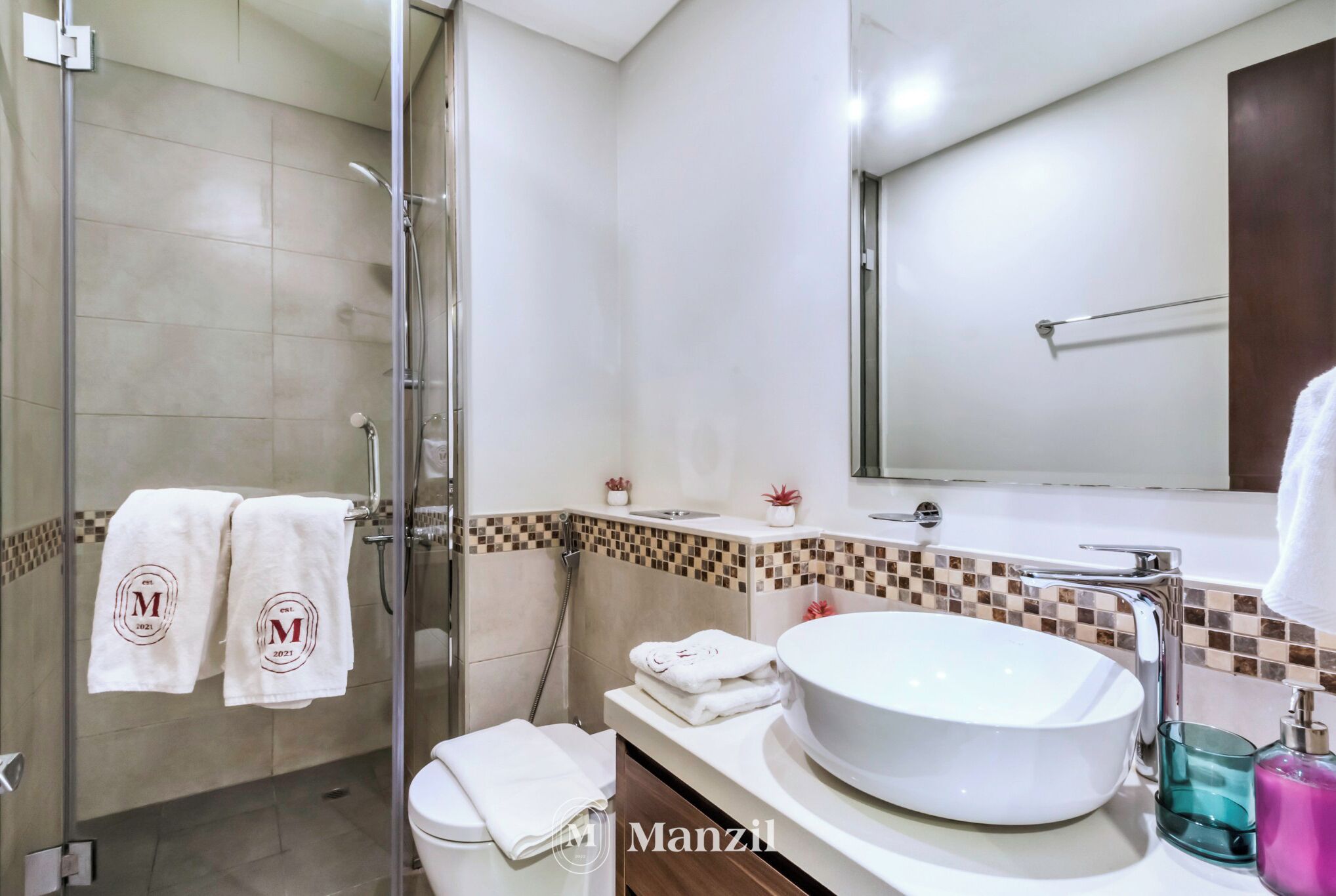 A modern bathroom with a glass shower enclosure, a white sink with a large basin, and a tiled shower area.