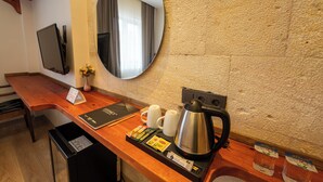 Hotellihuone, jossa on puinen työpöytä, kahvinkeitin, peili ja televisio.