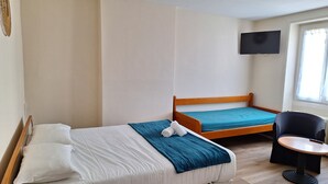 Une chambre d’hôtel avec deux lits simples, un téléviseur fixé au mur, une petite table et une chaise.