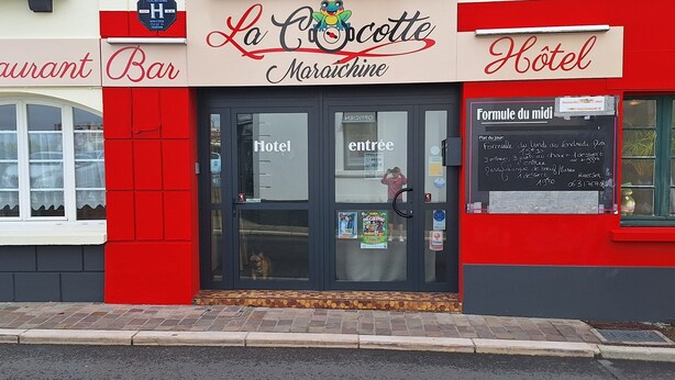 Un bâtiment à la façade rouge et blanche, sur laquelle on peut voir des enseignes indiquant la présence d’un bar, d’un restaurant et d’un hôtel.