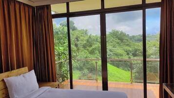 Un dormitorio con una ventana grande, una cama y vistas a un paisaje verde.