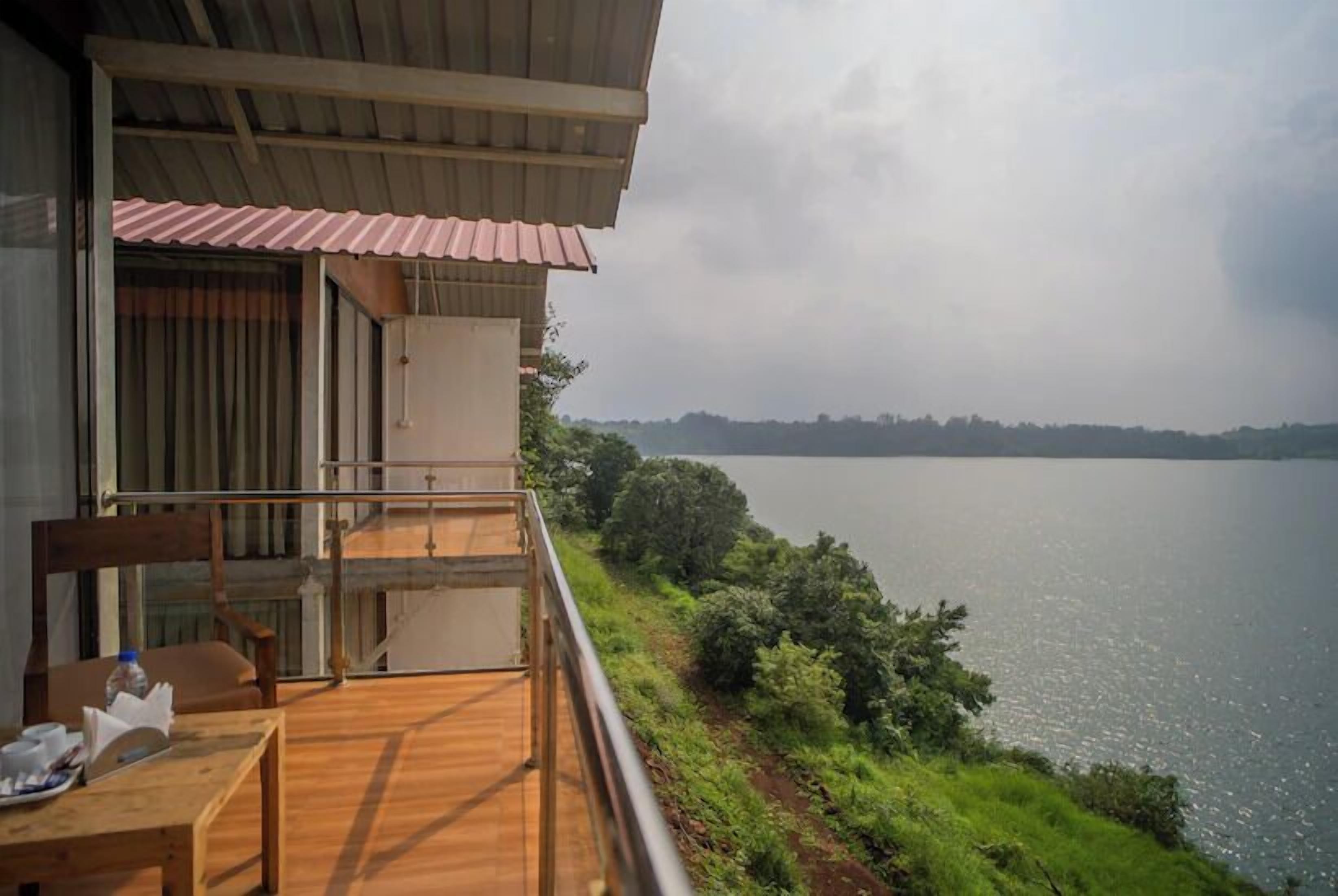 A balcony with a wooden table and chairs, overlooking a body of water and greenery.
