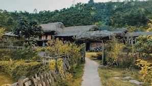 A rural village with thatched-roof houses, a dirt path, and lush greenery. - Ban Lien Pine Homestay Lao Cai (Ban Lien)