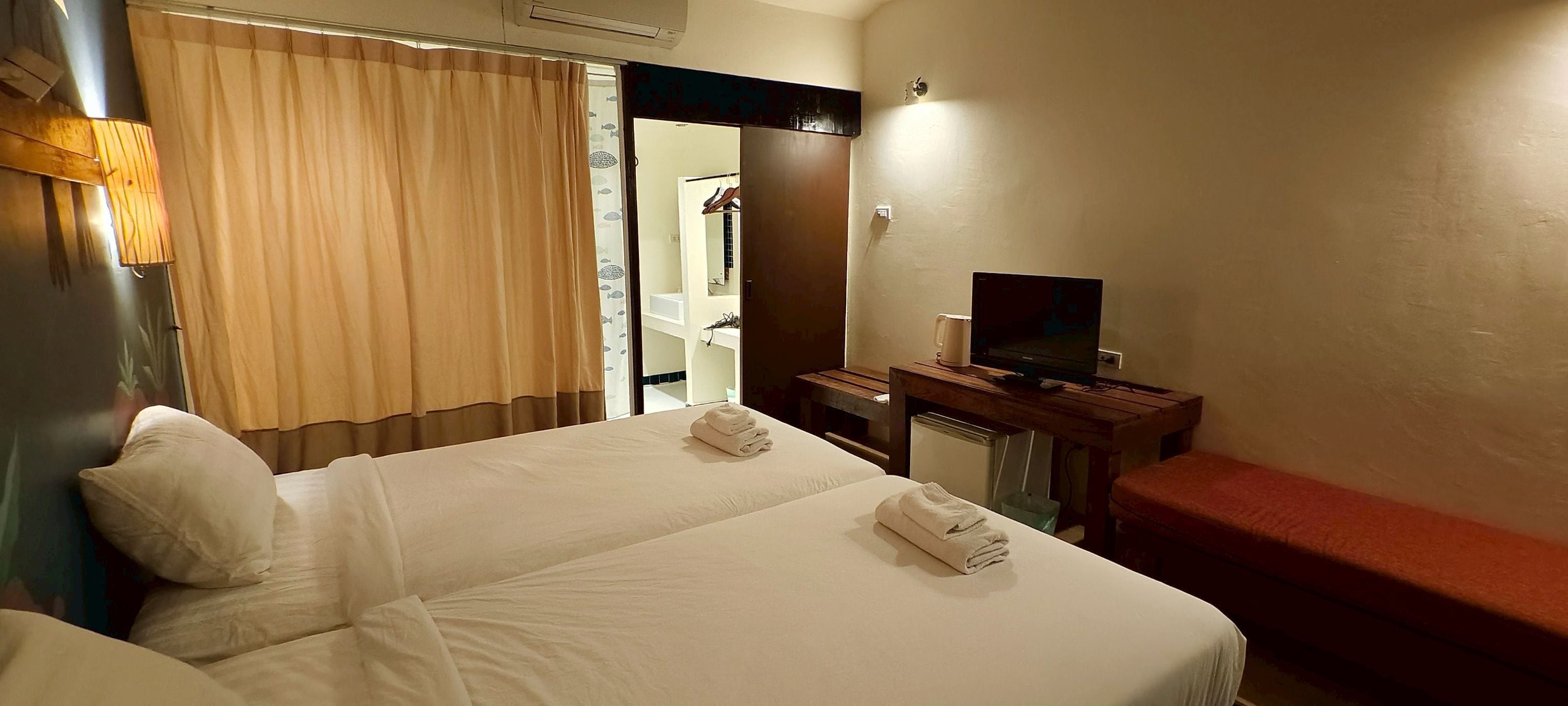 Habitación de hotel con dos camas, televisión, escritorio y baño visible a través de una puerta abierta.