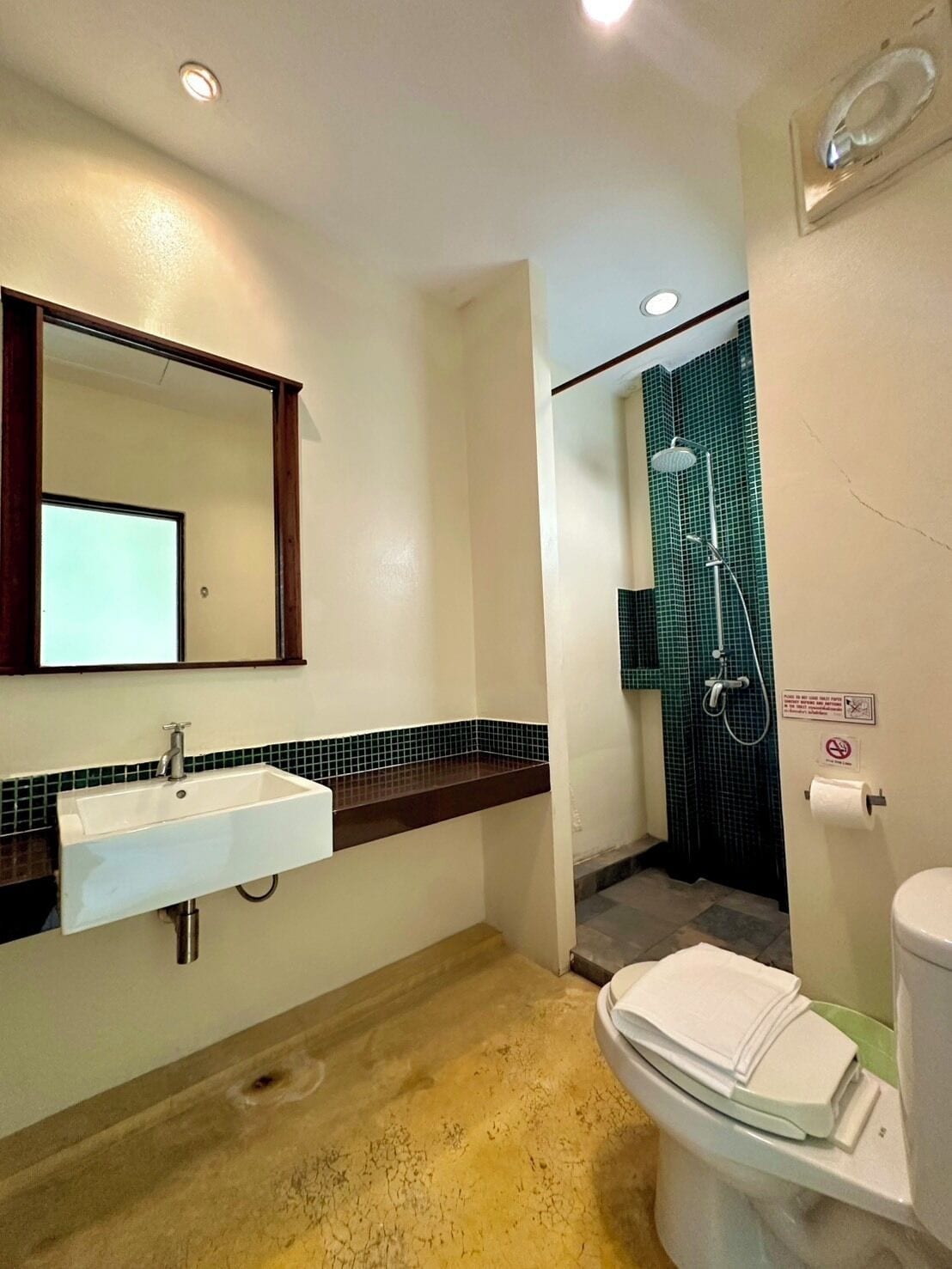 A bathroom with a sink, mirror, shower, toilet, and a sign indicating no smoking.