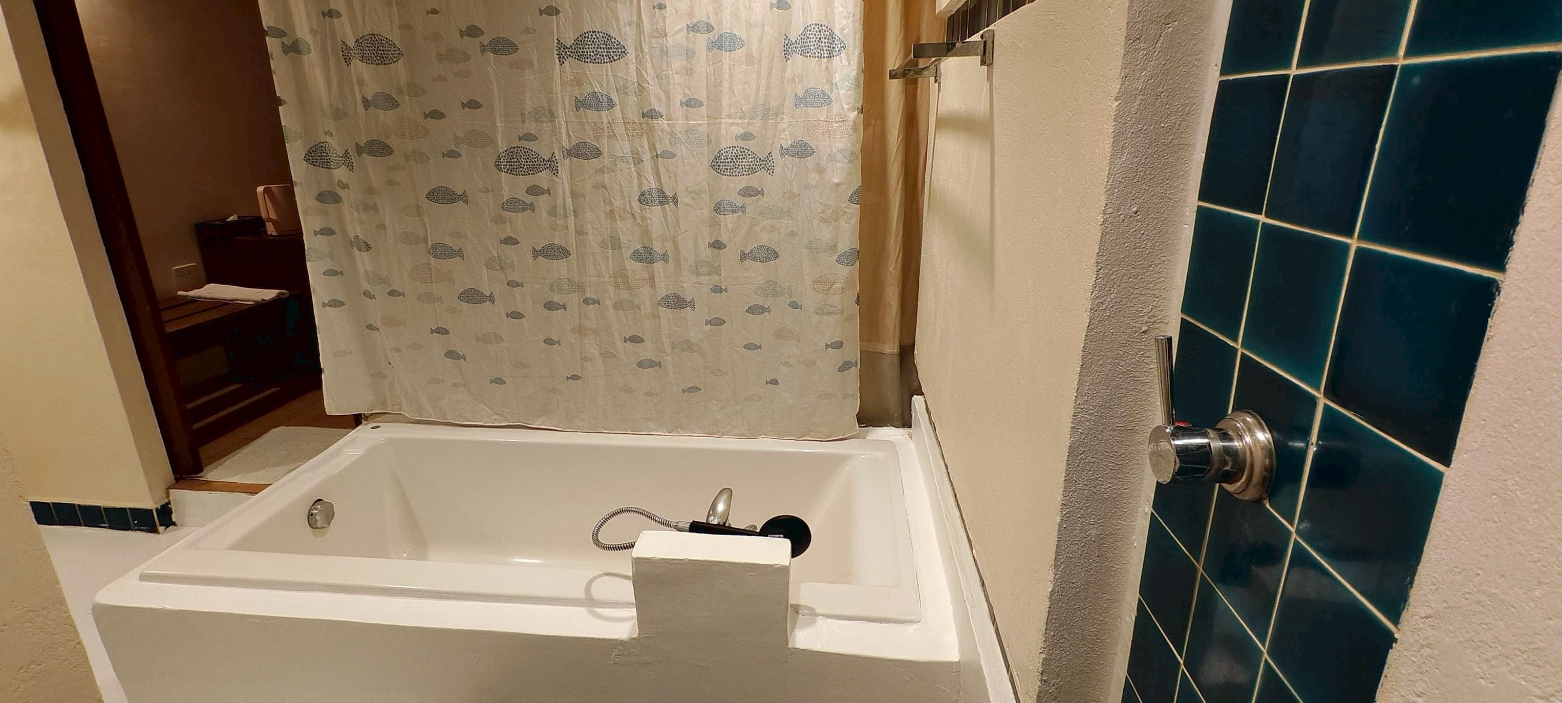 Un baño con bañera, cortina de ducha con motivos de peces y paredes con azulejos azules.